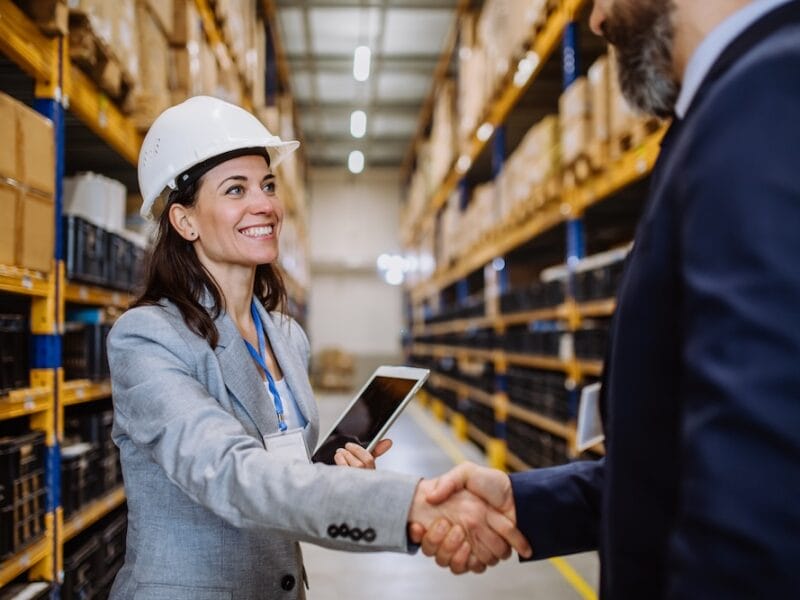 Managers in suits shaking hands in a warehouse.