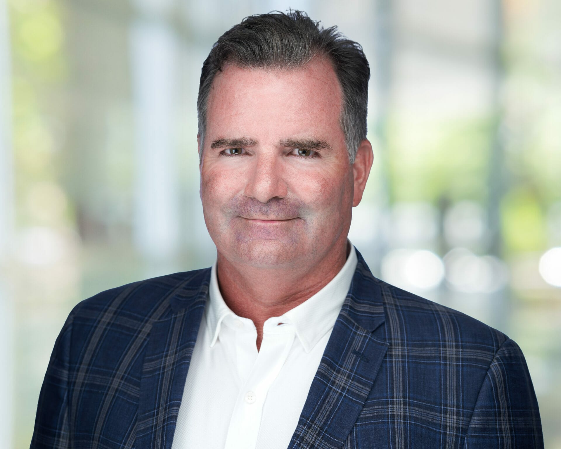 A man in a navy blue checkered suit jacket and white shirt posing for a professional headshot
